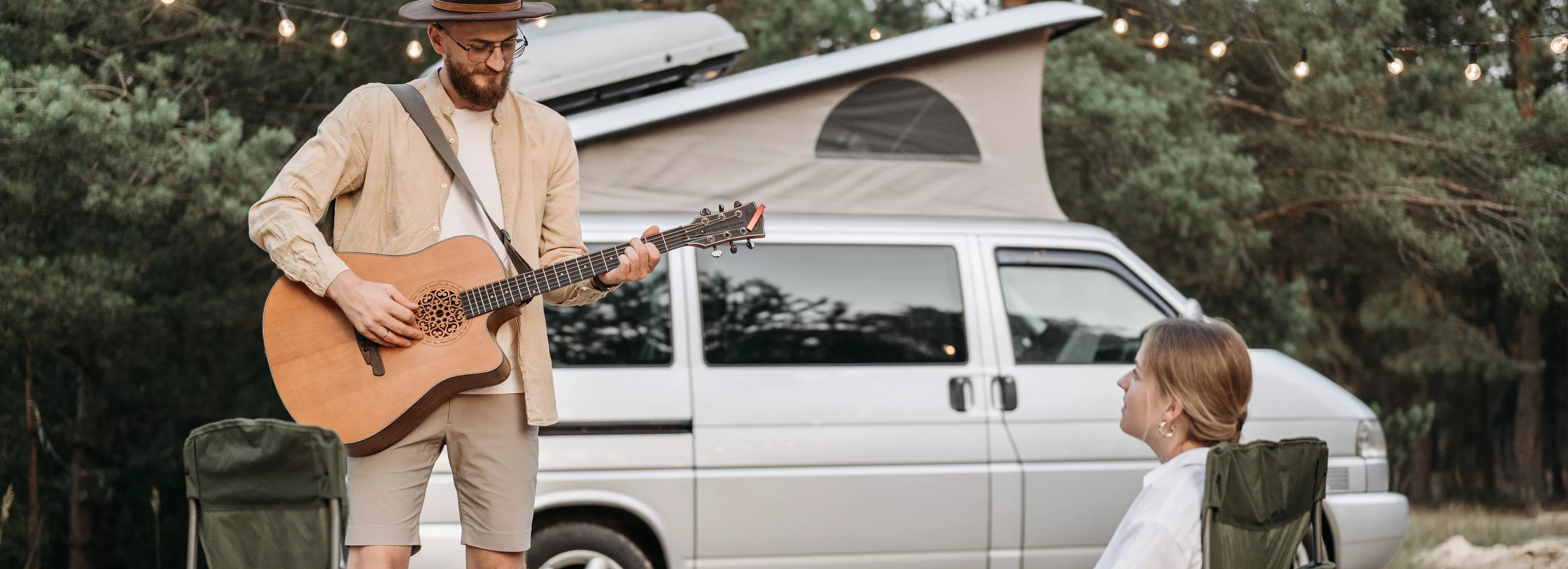 Campervan mit Hochdach im Hintergrund und Mann spielt Gitarre